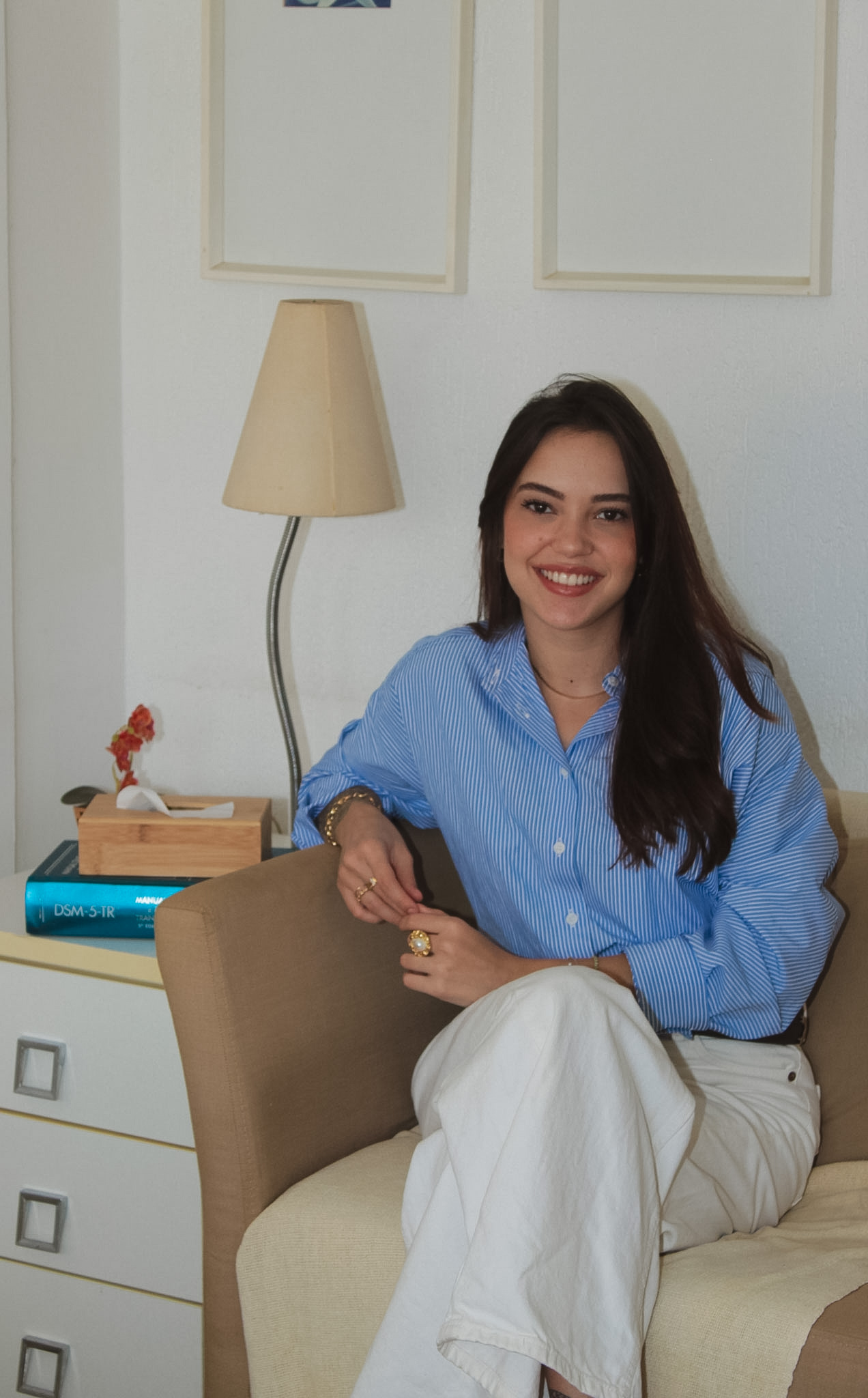 Maria Victória sentada na poltrona do consultório, ao lado de uma luminária e de livros de psicologia
